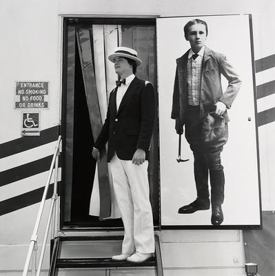 [young man standing in a doorway with a blown-up old fashioned photo of a boy on right]