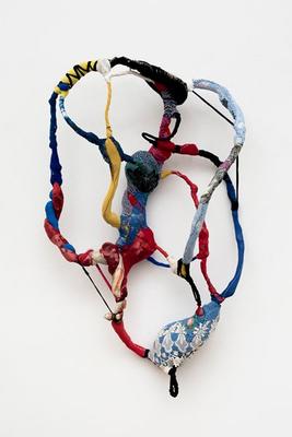 thin tubes of multicolored fabric forming an oblong shape, braces by thin black pieces of fabric at sides; thicker shape at bottom in blue fabric with lace on it, and a pink flower; red and blue entwined tubes of fabric at PL; green fabric with a black flower in C